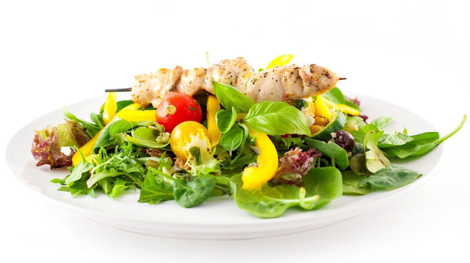 Grilled chicken salad with mixed greens and peppers on a white plate